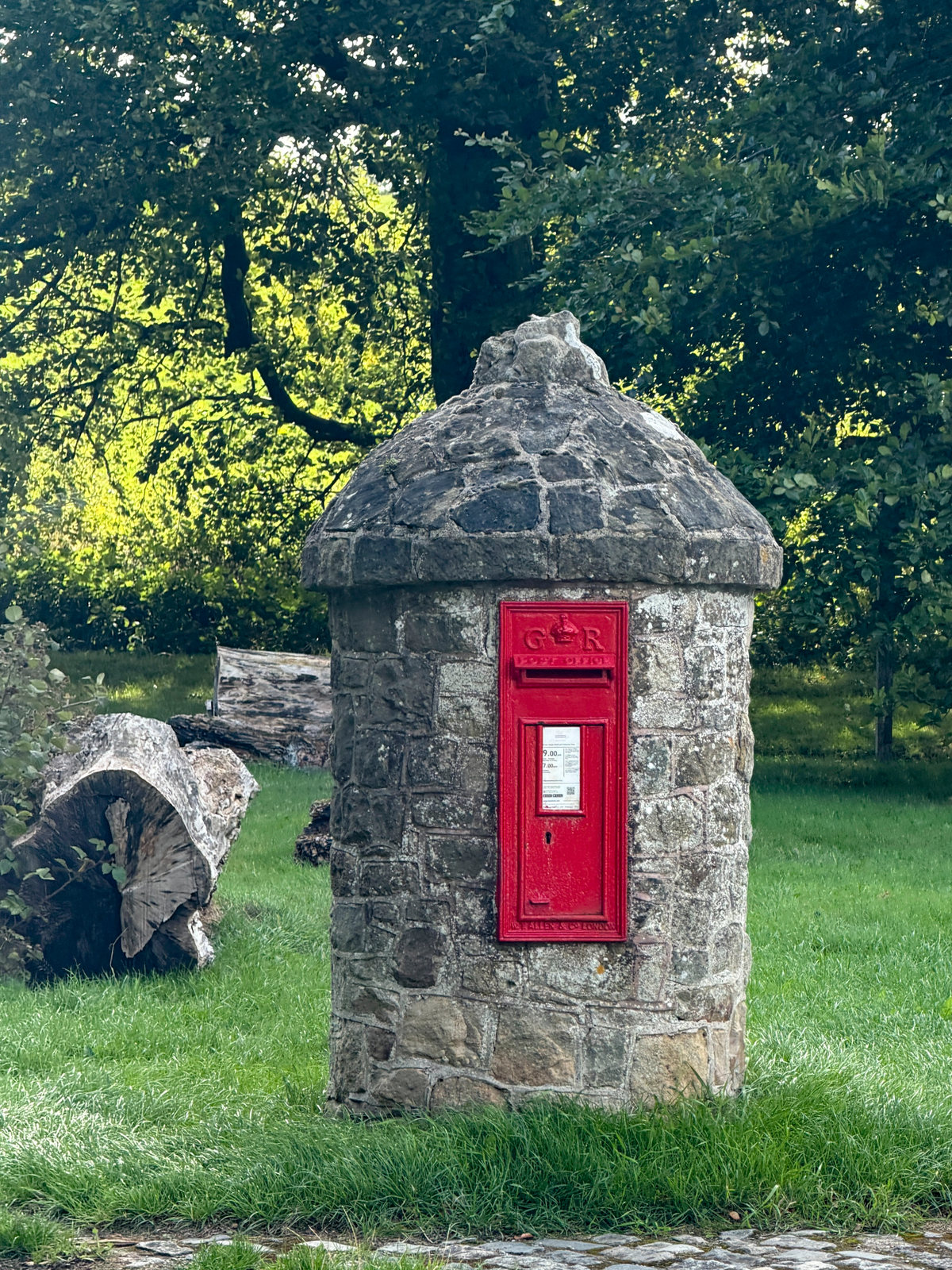 A red postbox set into a small stone structure beside a wall.