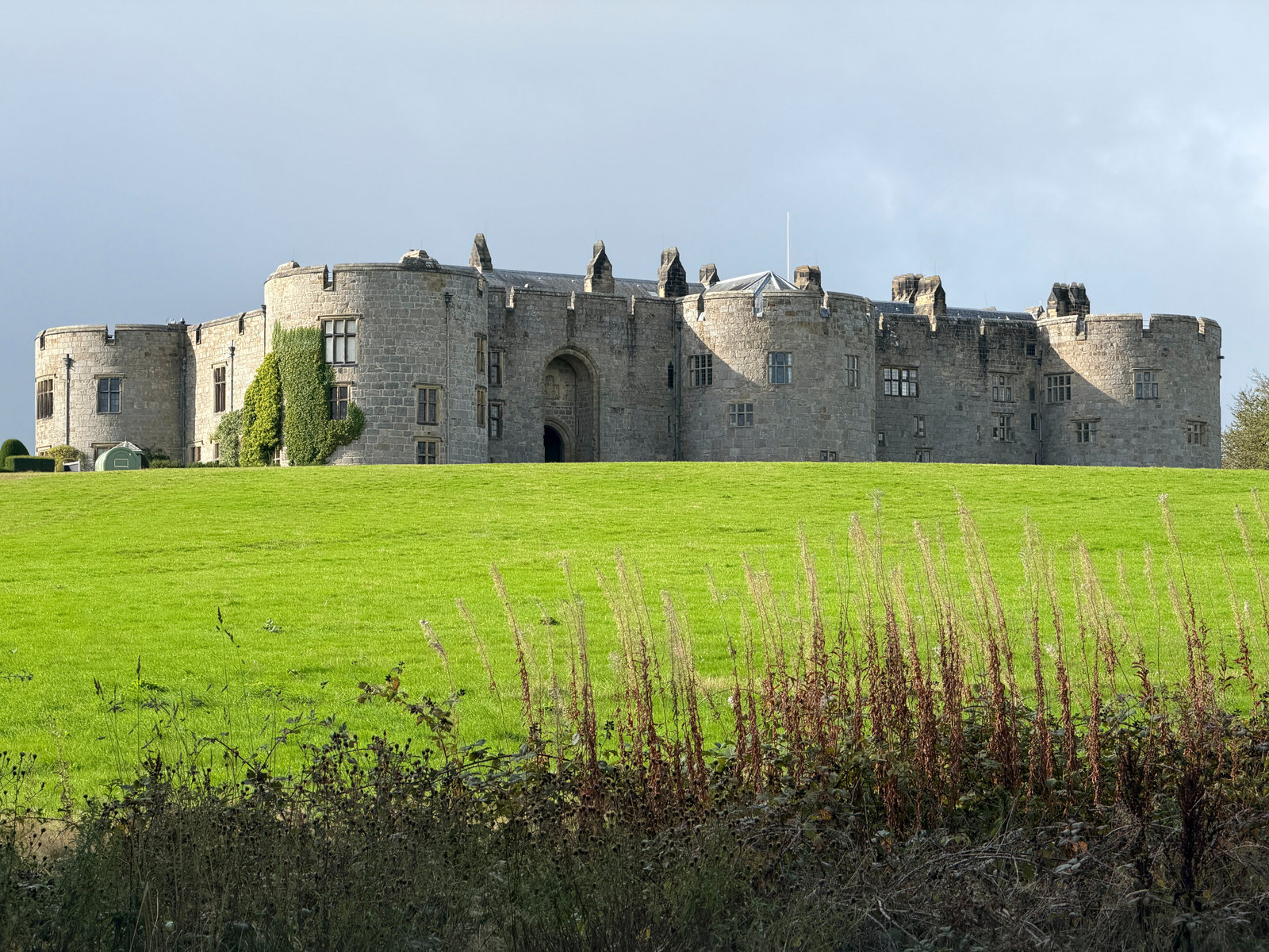The stone frontage and round towers of Chirk Castle across a green field.